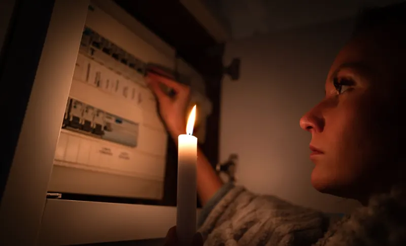 Vrouw bij meterkast met kaars tijdens stroomstoring, spoed elektricien